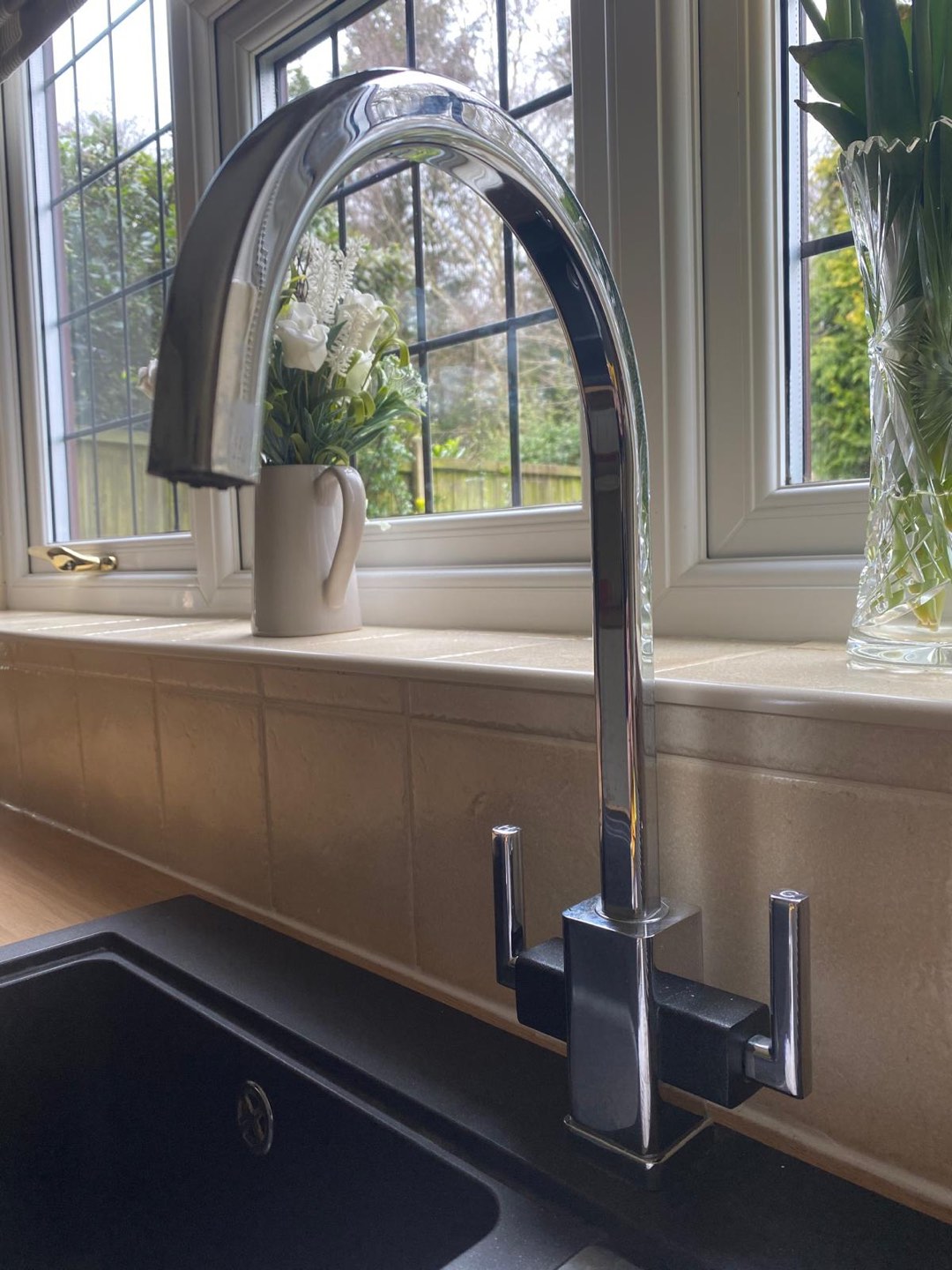 Chrome swan-neck tap over a black kitchen sink with marble-tiled splashback and leaded bay window